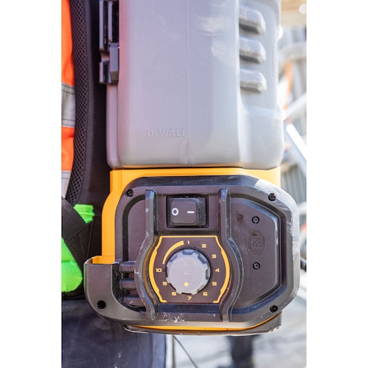 Close-up view of a DEWALT device control panel featuring a power switch and a numbered dial, worn by a person in high-visibility work clothing.