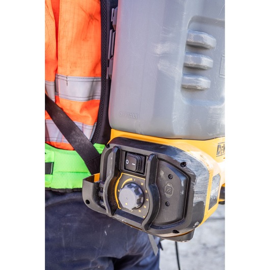 Close-up of a DEWALT portable power tool with a control knob and power switch, worn on the side of a person dressed in high-visibility safety clothing.