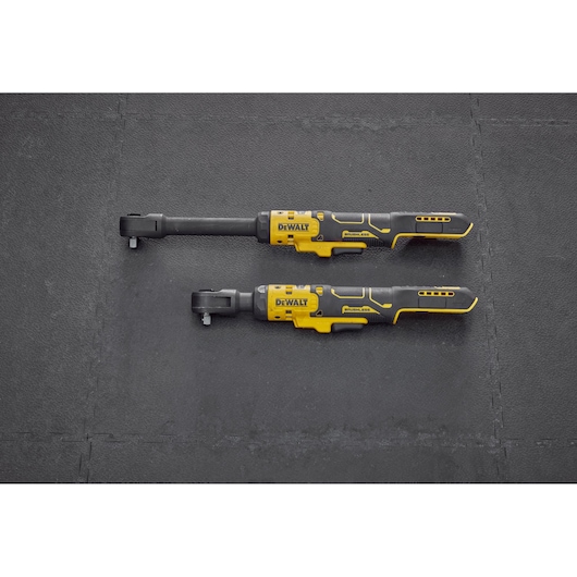 Two DEWALT cordless ratchet wrenches with yellow and black handles are displayed side by side on a dark textured surface. One tool has a longer shaft than the other.