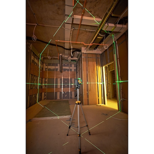 A DEWALT laser level mounted on a tripod projecting green laser lines across a room under construction, indicating alignment and leveling for installation work.